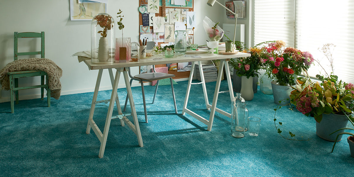 Ein blauer Teppichboden in einem Zimmer mit einem Tisch und Blumen. Raumausstattung Merget | Goethestraße 43 | 63814 Mainaschaff